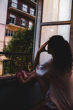 Aylık kız pencereden dışarı bakıyor. Balkona yaslanıyor.