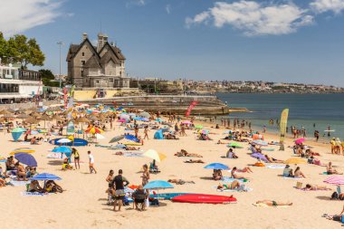 Portekiz, Lizbon yakınlarındaki Cascais 'de güneşli bir yaz haftasonu geçiren yerliler ve turistlerle dolu bir plaj.