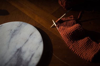 Okunmuş turuncu örgü mermer kaplamalı ahşap masada oturuyor. 