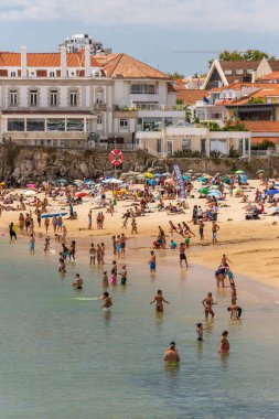 Portekiz, Lizbon yakınlarındaki Cascais 'de güneşli bir yaz haftasonu geçiren yerliler ve turistlerle dolu bir plaj.