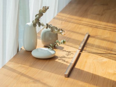 Bir grup beyaz seramik vazo küçük fren ve ağaç yaprakları ile mat ahşap masa yüzeyinde doğal ışık ile.