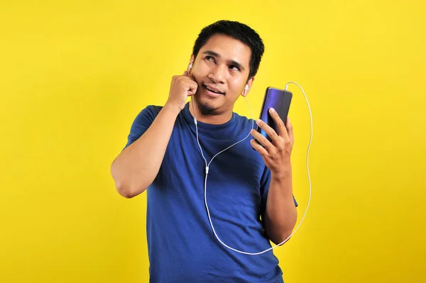 在智能手机上听音乐的亚洲人看着被黄色背景隔离的复制空间 — 图库照片