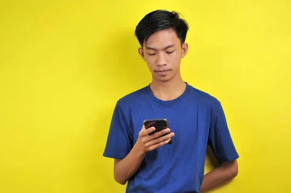 黄色の背景に隔離されたスマートフォンを使用して深刻なアジアの男の肖像画 — ストック写真