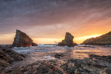 Karadeniz 'in kayalık kıyı şeridinde renkli gündoğumu gökyüzü ile fırtınalı bir deniz..