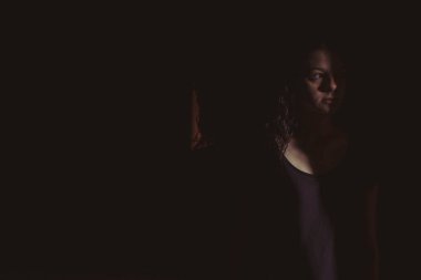 Siyah arka planda genç bir kadın, yüzünde ışık ve gölgeler var.