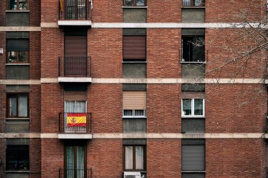 İspanyol bayrağı, İspanya 'da Madrid caddesinde tuğla ön cepheli ve pencereli çok katlı bir apartmanın küçük balkonunda asılı.
