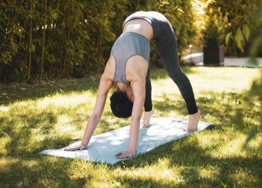Bahçede minderle yoga yapan genç bir kız.