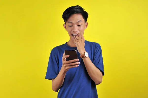 身穿白衬衫的亚洲男人吓得满脸通红 看着黄色背景的手机屏幕 — 图库照片