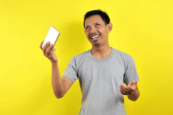 Zabawny Młody Azjata Trzyma Smartfona Odizolowany Żółtym Tle — Zdjęcie stockowe