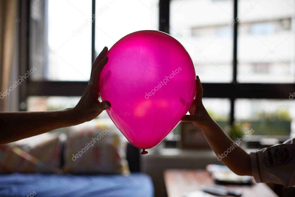 A woman's hand and a child's hand hold a pink and balloon.