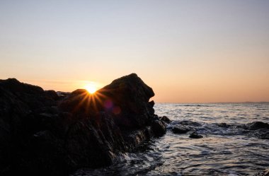 Atlantik Okyanusu 'nun arka planında günbatımı olan kayanın üzerindeki güneş patlaması, Punta Ballena, Maldonado, Uruguay