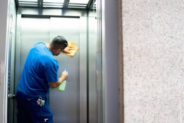 maintenance personnel disinfecting the elevator walls to avoid covid19 clipart