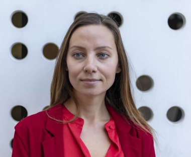 Kırmızı ceketli genç sarışın kadın caddede yürüyor.