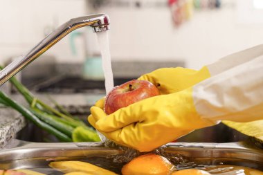 Manzarayı kapat. Coronavirus için lateks eldivenle meyve ve sebze temizleme.