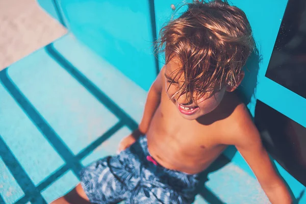 Boy sitting and laughing at the blue lifeguard tower at the beach