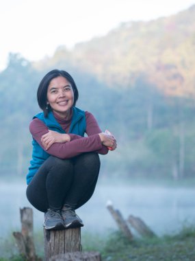One asian lady squat on wooden pole near the lake in the park.