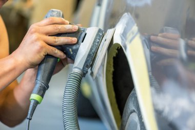 Araba tamirhanesinde araba cilalayan bir adamın elinde öğütücü..