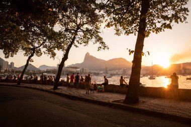 Günbatımında sosyalleşen insanlarla Urca okyanus kıyısına güzel bir manzara ve arkasında Corcovado dağı, Guanabara Körfezi, Rio de Janeiro, Brezilya