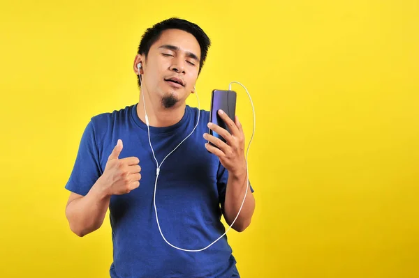 亚洲人的画像 他们用闭着眼的智能手机听音乐 背景是黄色的 — 图库照片