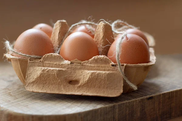 Close up egg carton of half dozen with a rope, beige tones, above a kitchen table. Horizontal view and a symmetrical.