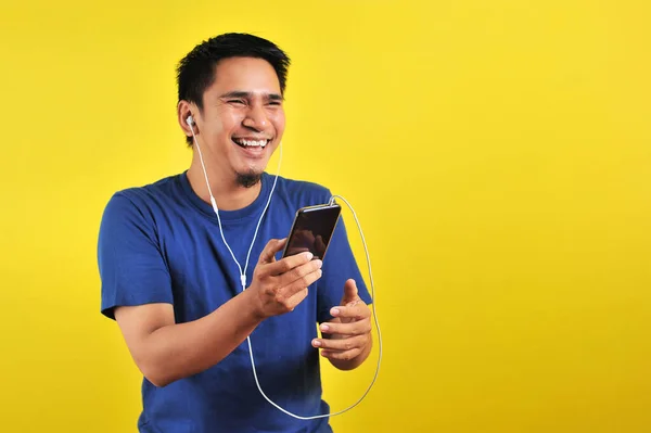 兴奋的亚洲男人听着智能手机里的音乐 在黄色背景下被隔离 开心地笑着的画像 — 图库照片