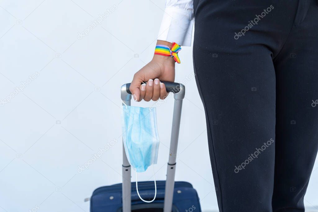 woman's hand with lgbt bracelet, suitcase and mask