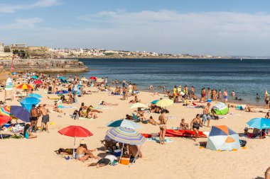 Portekiz, Lizbon yakınlarındaki Cascais 'de güneşli bir yaz haftasonu geçiren yerliler ve turistlerle dolu bir plaj.