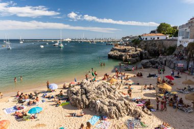 Portekiz, Lizbon yakınlarındaki Cascais 'de güneşli bir yaz haftasonu geçiren yerliler ve turistlerle dolu bir plaj.