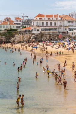 Portekiz, Lizbon yakınlarındaki Cascais 'de güneşli bir yaz haftasonu geçiren yerliler ve turistlerle dolu bir plaj.