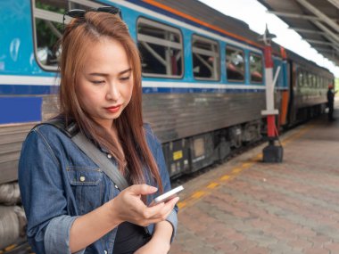 Tren peronunda arkasında tren olan akıllı telefonlar kullanan Asyalı kadınlar. Tren istasyonunda akıllı telefondan bilgi arayan Asyalı genç bir bayan..