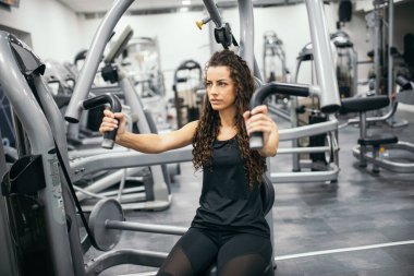 Odaklanmış genç bir kadın spor salonunda egzersiz yapıyor.