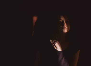 Siyah arka planda genç bir kadın, yüzünde ışık ve gölgeler var.