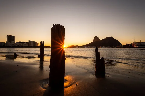 Beautiful sunrise light and view to Sugar Loaf Mountain with wooden stumps of old pier in Botafogo Beach, Rio de Janeiro, Brazil