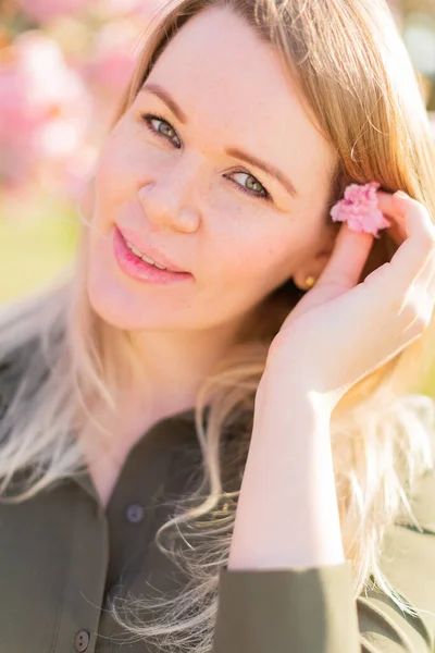 Freckled blonde pregnant woman in the park at spring with sakura trees, shallow depth of field pregnancy glow