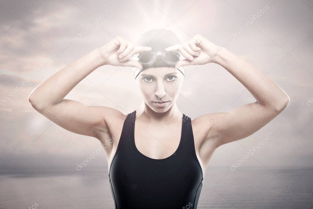 Young athletic swimer woman with googles and swimming cap, with the ocean in the backgroun