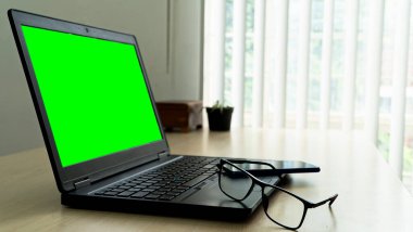 Yeşil ekran gözlüklü, ahşap masadaki dizüstü bilgisayar ve bulanık arka planlı akıllı telefon.