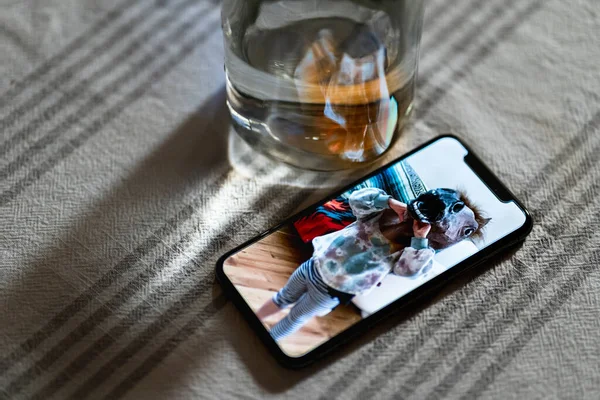 智能手机展示了小孩戴着橡胶马面具坐在一杯水旁边的照片 — 图库照片