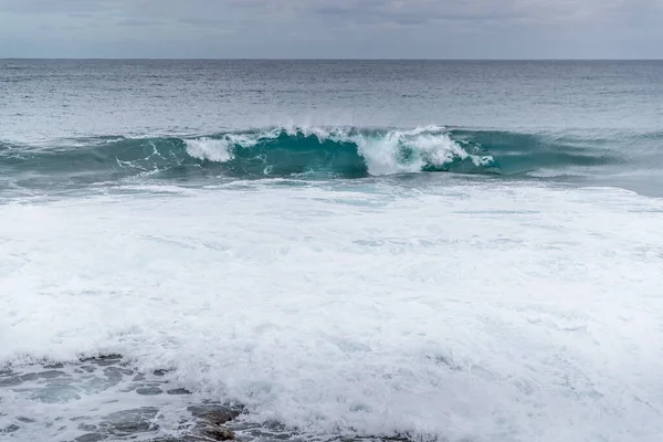 波が岩だらけの海岸に衝突し 海の地平線に係留されたボートのペアで側面に跳躍する水を破壊する — ストック写真