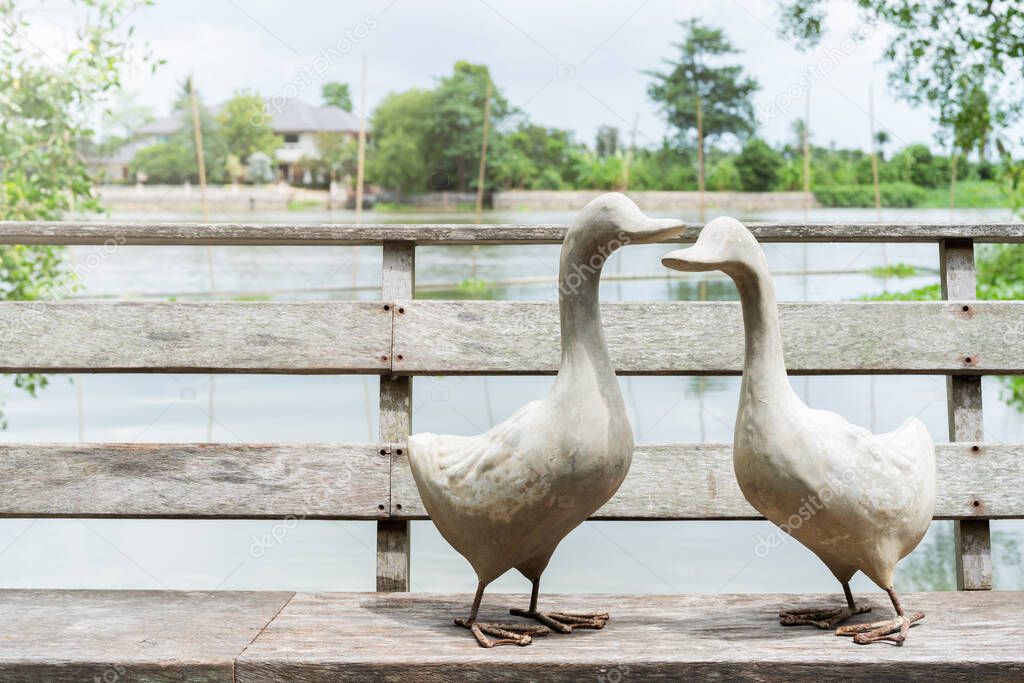 couple of white goose standing on wooden bridge near river, A statue of two goose on sunny day