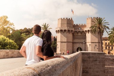 Couple observing the Serrano towers in the background, on the stone bridge. Young couple sightseeing in Valencia.