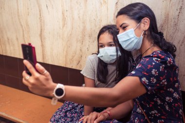 Yakın plan anne ve kızı akıllı telefonla fotoğraf çekiyor ve ameliyat maskesi takıyor. Metro istasyonunda kapalı mekan fotoğrafları..