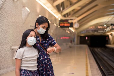 Genç bir kadın ve kızı treni bekliyor. İstasyonda tıbbi maske takan kızlar. Covid19 salgını sırasında seyahat kavramı.