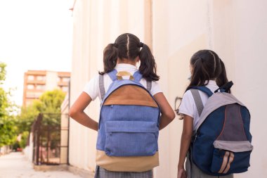Two little girls on rear view wearing backpacks on school, primary back to school concept.