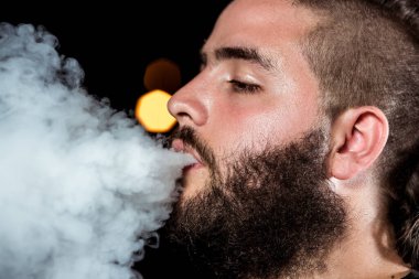 Close up face young man throw smoke through the mouth with a long beard