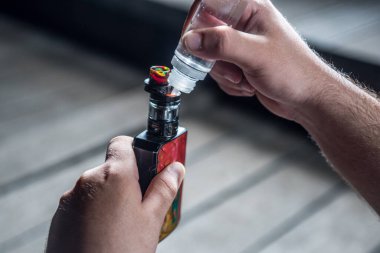 Nikotin kullanmadan sigara içmek için elektronik sigara dolduran bir adam. Makineye sıvı döken ellerin ayrıntıları