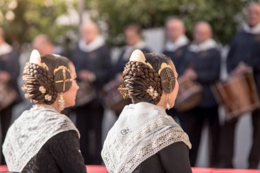 Valencia 'da halka açık bir yerde arkadan iki falleras görülmüş. Fallas 'ın tipik saç stilinin detaylı fotoğrafı. Arka planda müzisyenler bulanıklaştı.