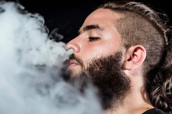Close up face young man throw smoke through the nose with a long beard