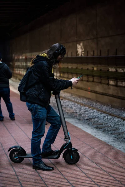 電話を見ながら電動スクーターで地下鉄を待っている男の子 — ストック写真