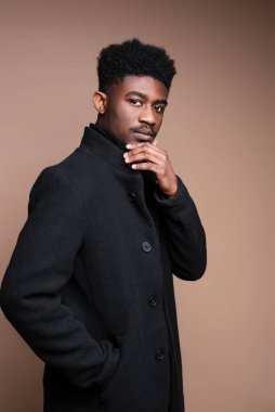 African man in black jacket looking at camera on beige background