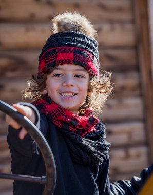 Joyful child in red plaid winter hat and scarf smiling outdoors